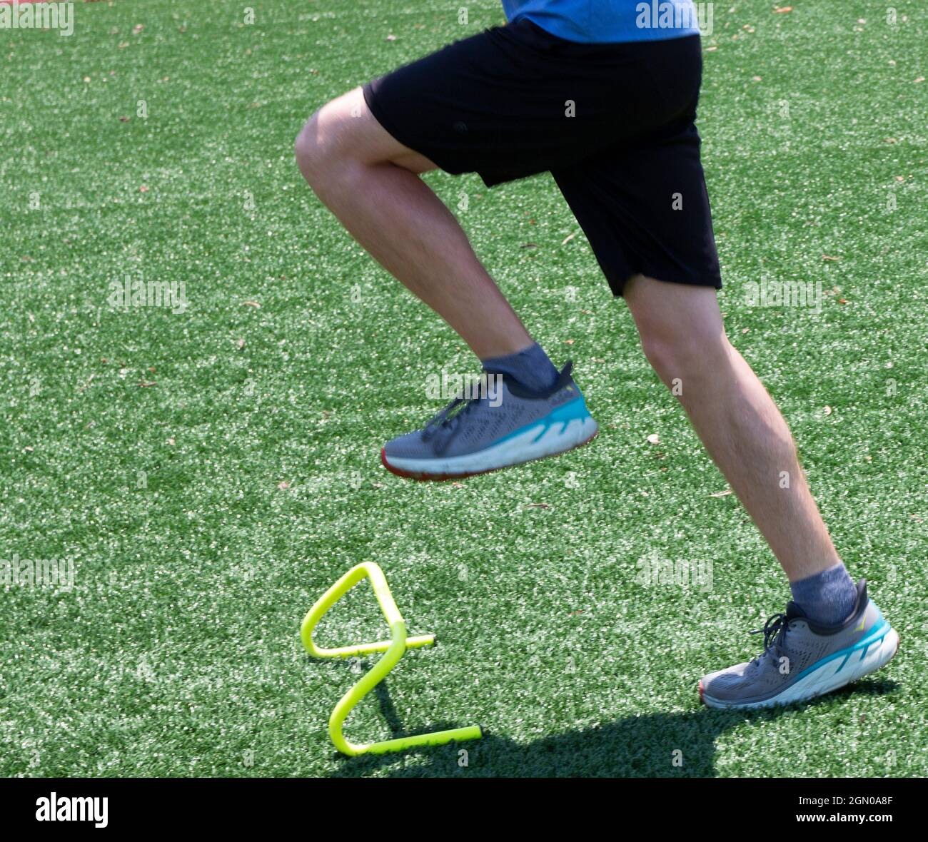 A high school track runner is stepping over yellow mini hurdles on a turf field practicing running form drills. Stock Photo