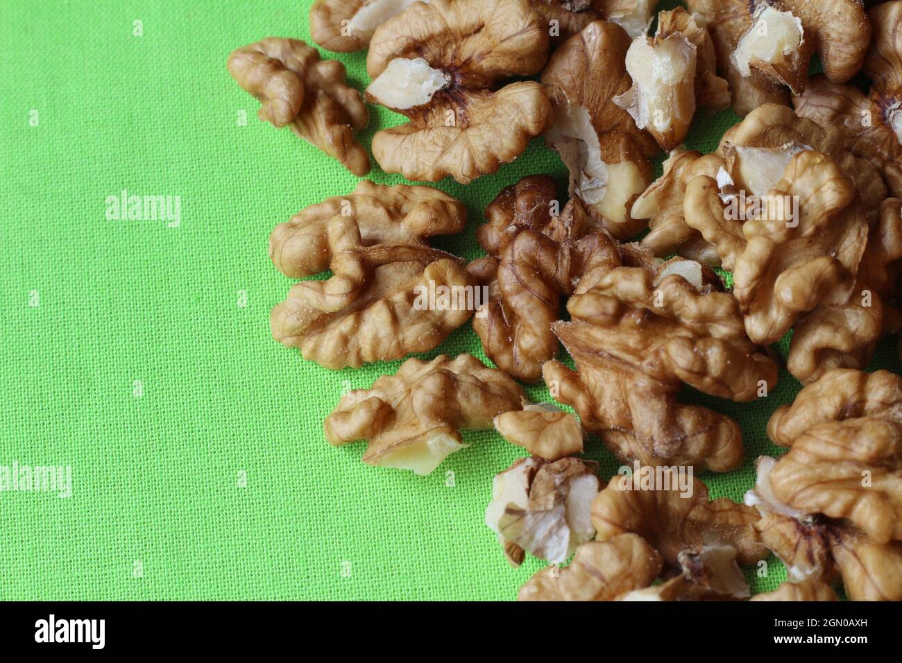 Top down view of shelled walnuts on a bright green table cloth. Nature food healthy snacks background, with copyspace to the left. Stock Photo