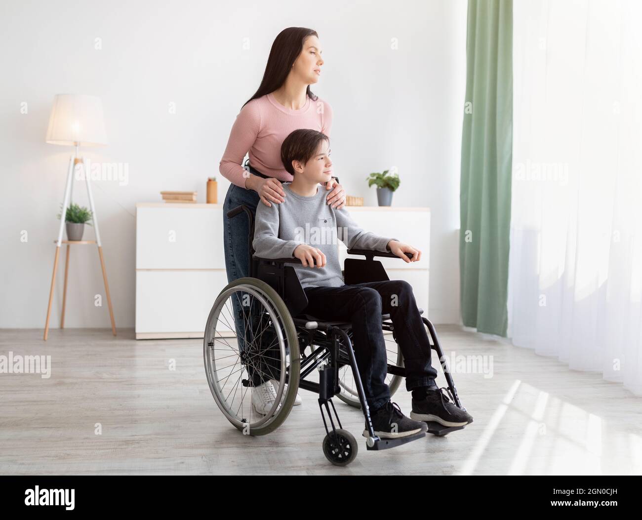 Full length of young mom and her impaired son in wheelchair looking out