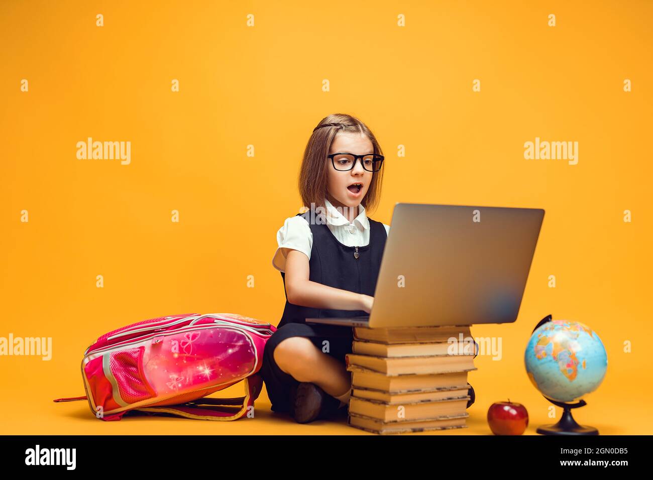 Full length surprised schoolgirl sitting behind a stack of books ...