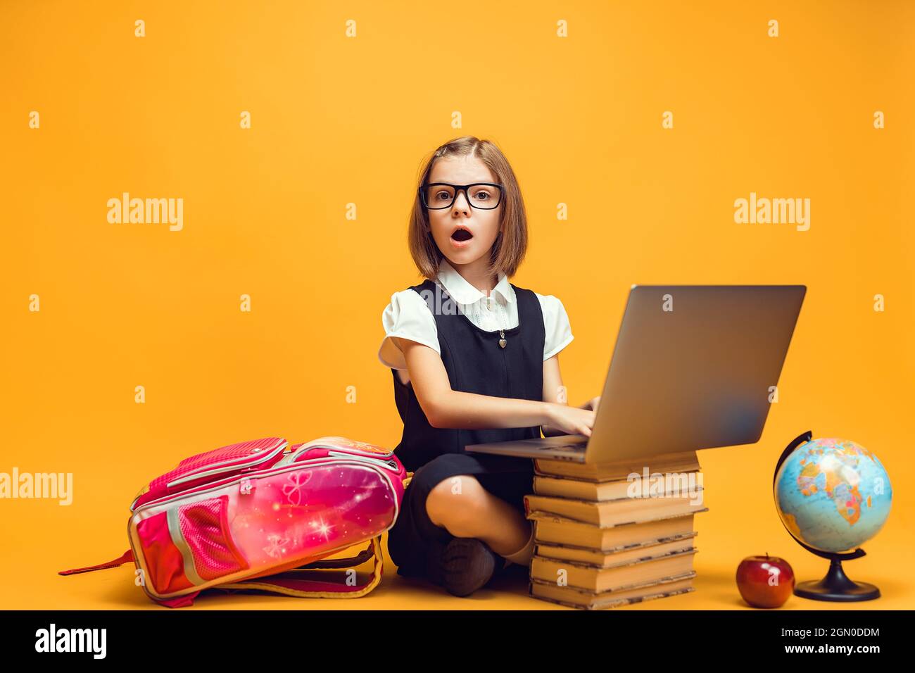 Full length surprised schoolgirl sitting behind a stack of books with ...