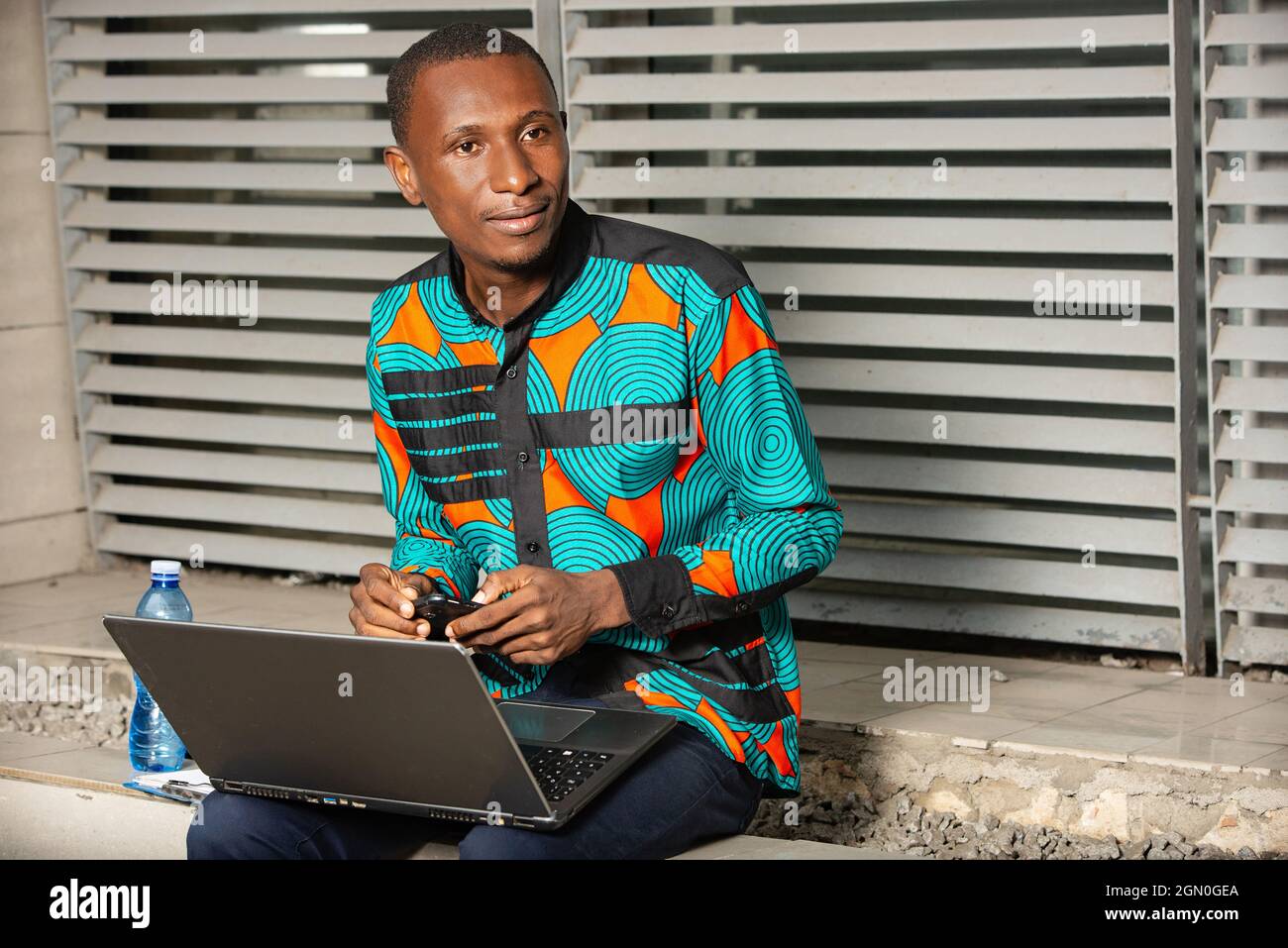 handsome african man sitting outside using a laptop and looking aside smiling Stock Photo