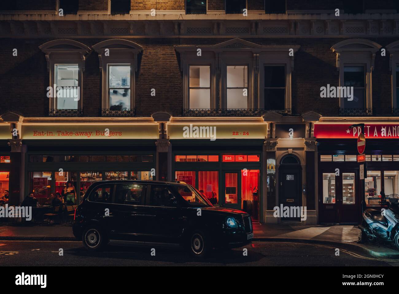 London, UK - September 03, 2021: Modern black cab with illuminated sign in front a restaurants on a street in London, UK. London taxis are an importan Stock Photo