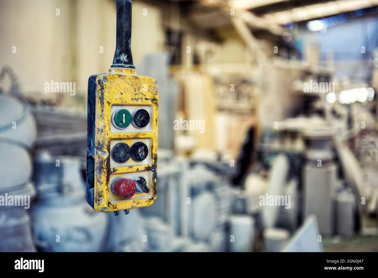 Weathered yellow controller with buttons for remote operating overhead crane hanging in industrial workplace with blurred equipment Stock Photo