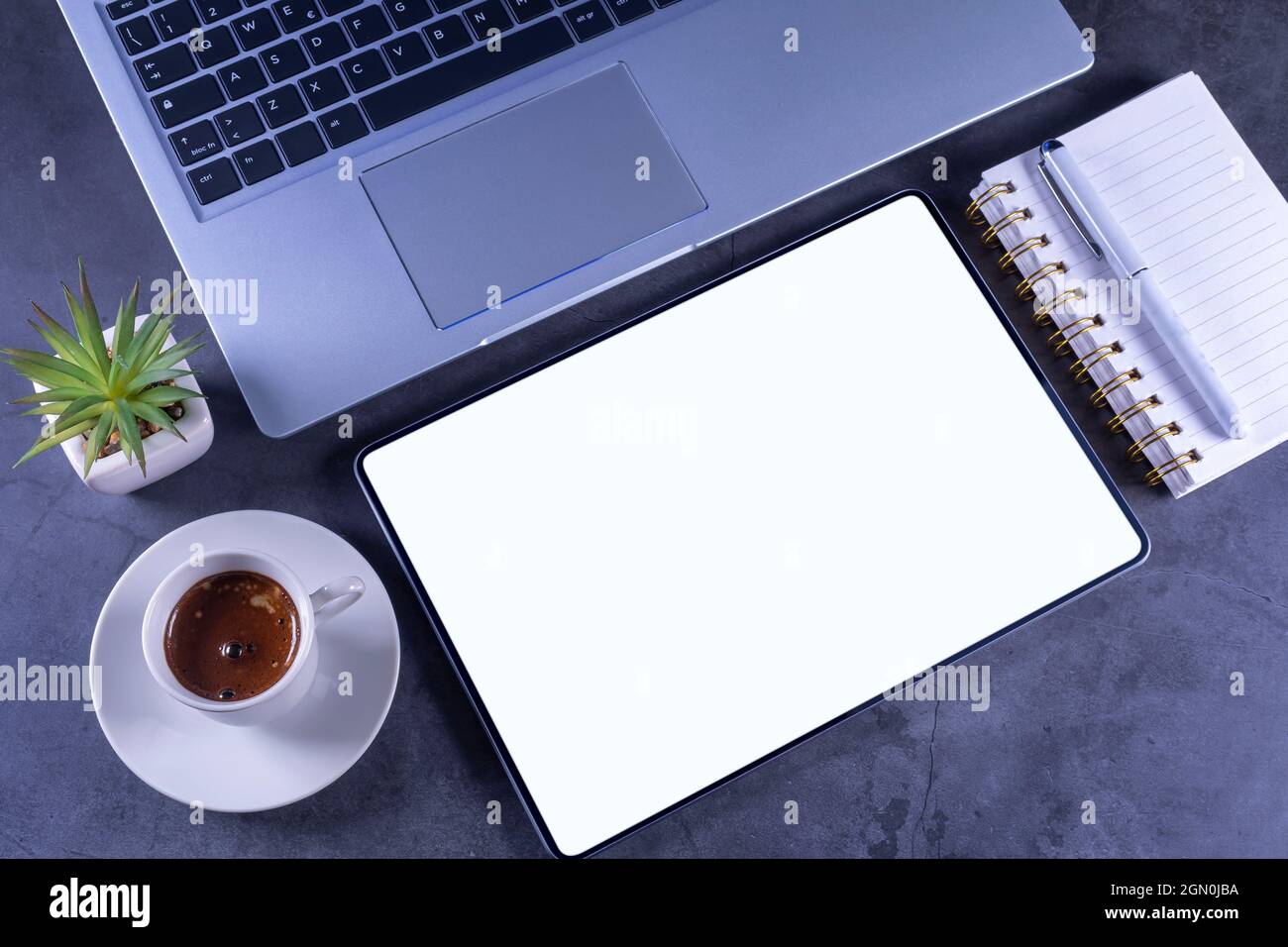 Tablet Pc with white blank screen over silver laptop with pencil, flower on desktop. Stock Photo