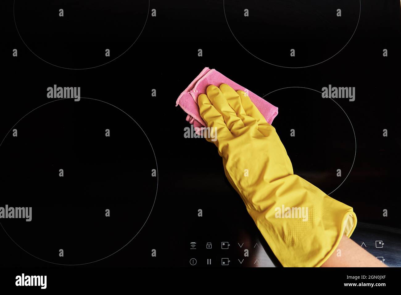 Cleaning induction stove. Woman in yellow rubber gloves cleans kitchen