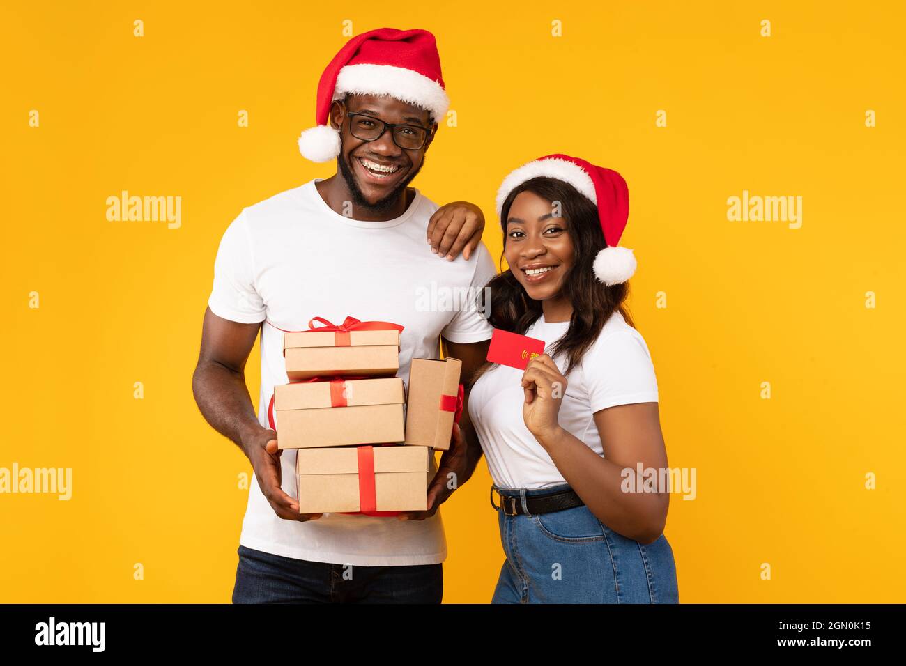 African Couple Holding Credit Card And Christmas Gifts, Yellow Background Stock Photo