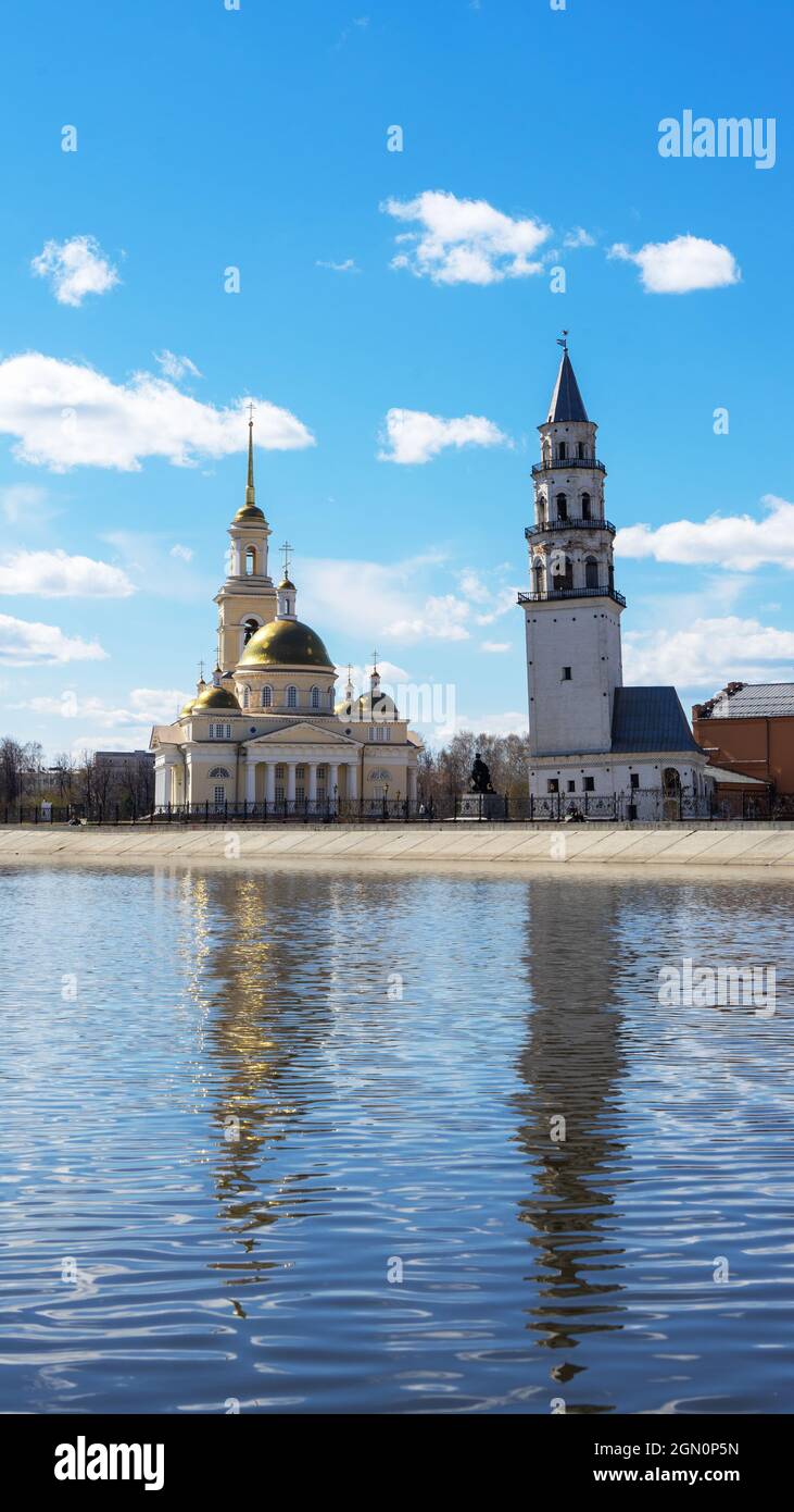 Leaning Tower of Nevyansk and Old Believers' church (domed) in spring day on the shore of the pond in Sverdlovsk Oblast, Russia. Vertical shot. Stock Photo