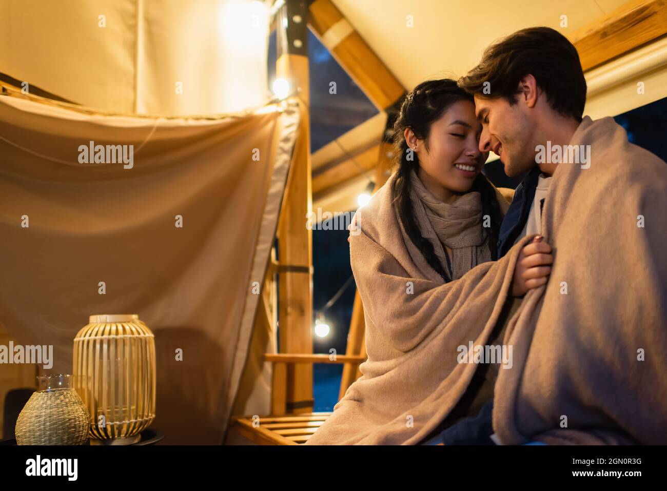 Asian woman hugging boyfriend in blanket on terrace of glamping house ...