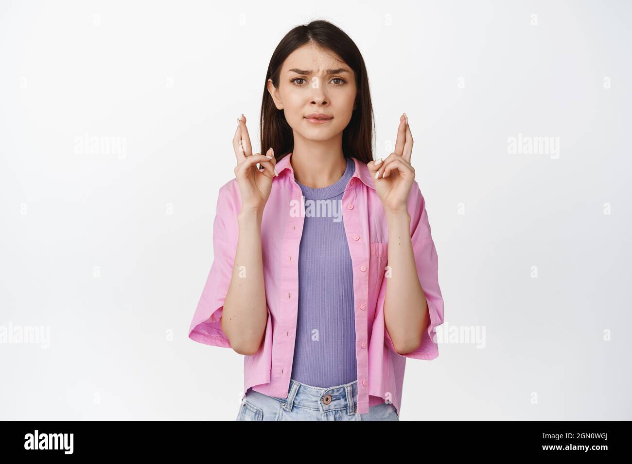 Nervous girl holds fingers crossed looking worried and prays makes wish stands against white background Stock Photo Alamy