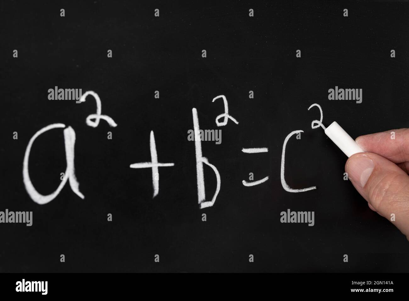 A teacher writes the Pythagorean theorem equation on a black chalkboard while teaching a group of students in a classroom. Stock Photo