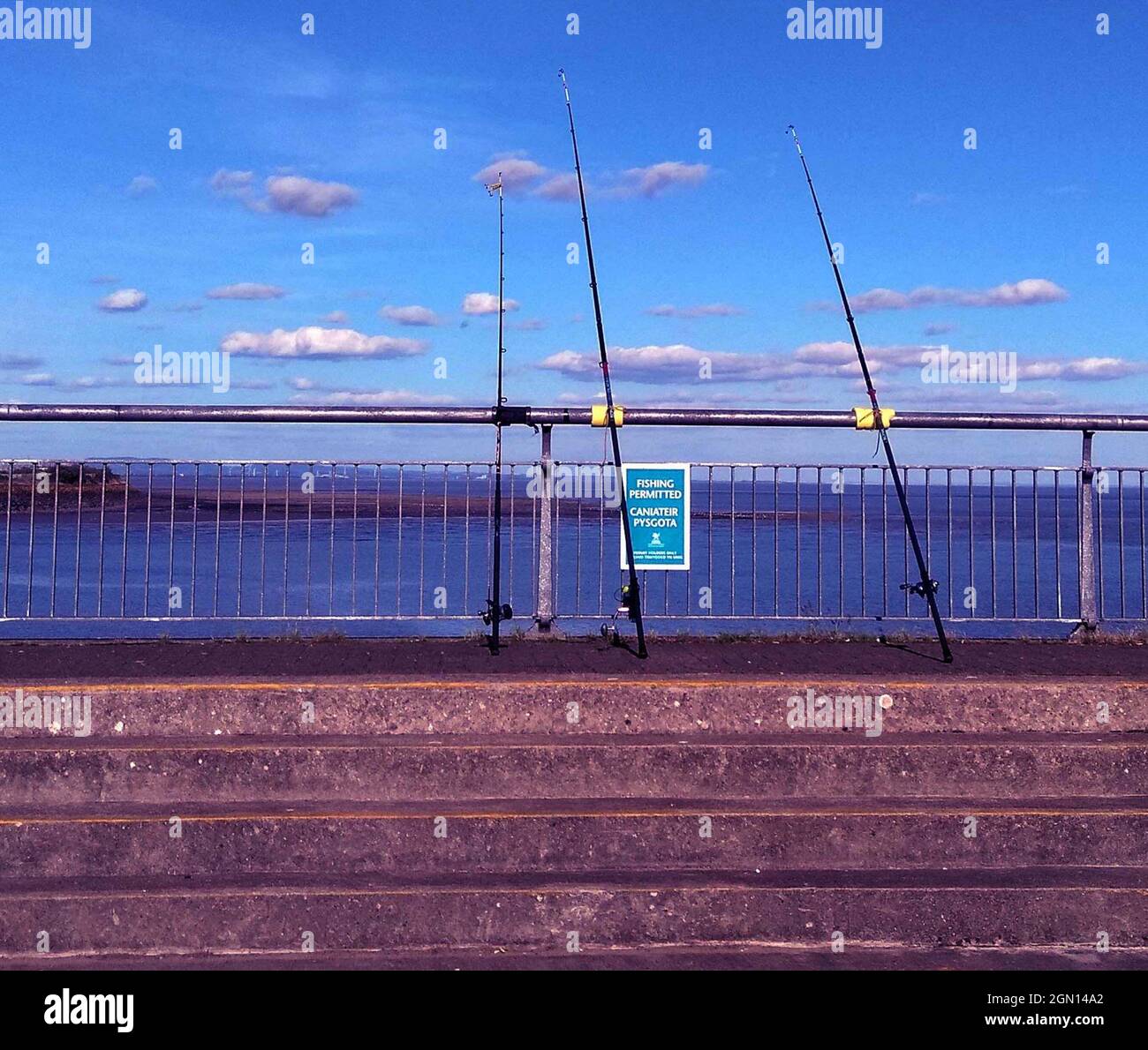Three Fishing rods resting on railings on Cardiff Bay barrage, Cardiff, Wales, UK Stock Photo