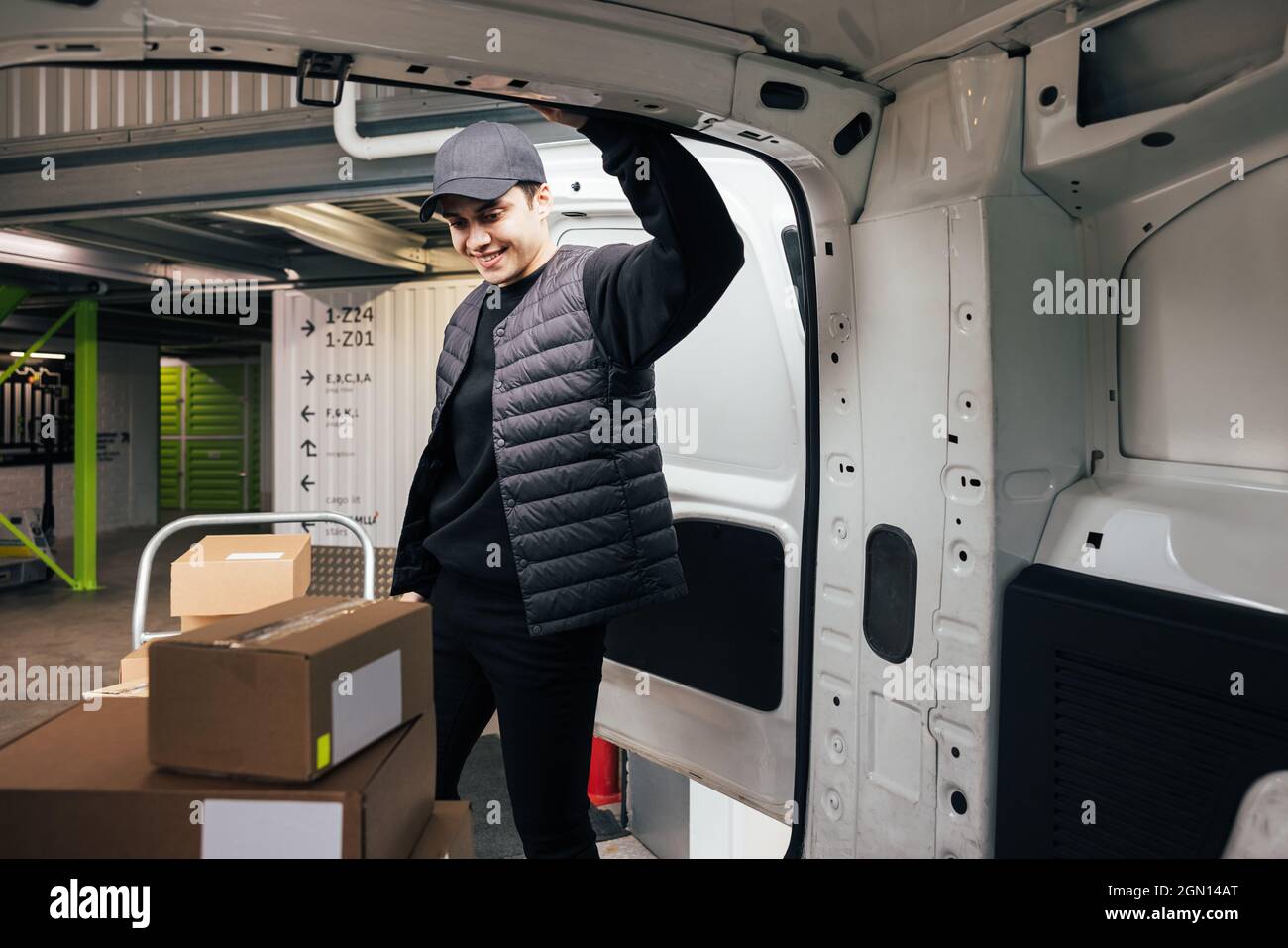 Confident courier leaning on van looking on cardboard boxes Stock Photo