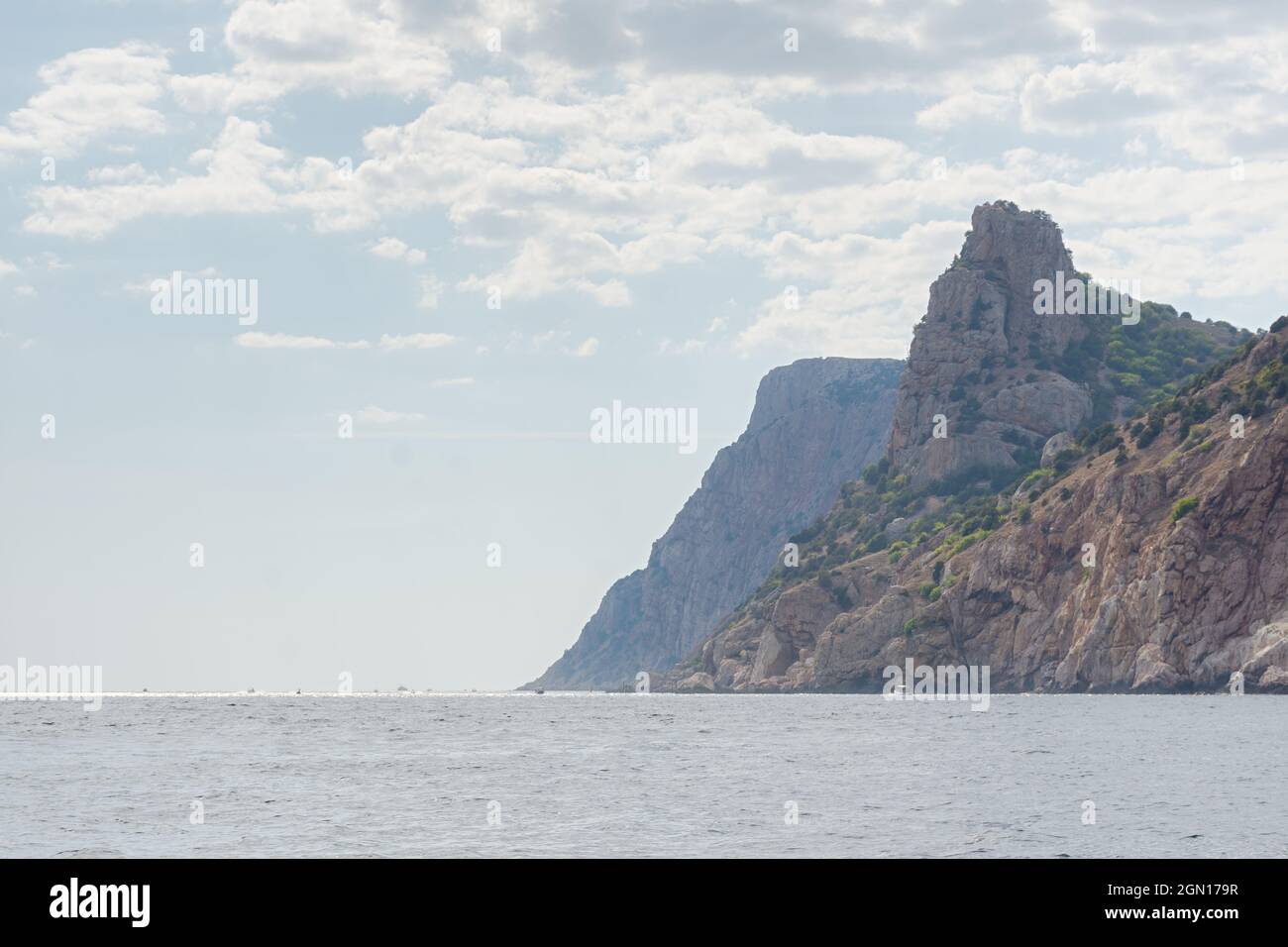 Mountains sea light. Light atmospheric summer seascape. View from the ship to the high cliffs with green trees, blue sky and small boats. The concept Stock Photo