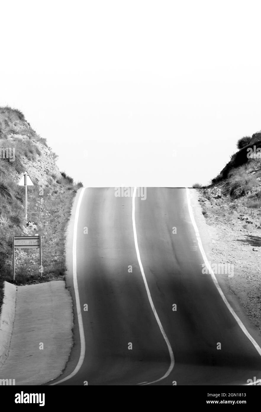 Lonely dizzying road with traffic sign in Spain. Monochrome picture Stock Photo