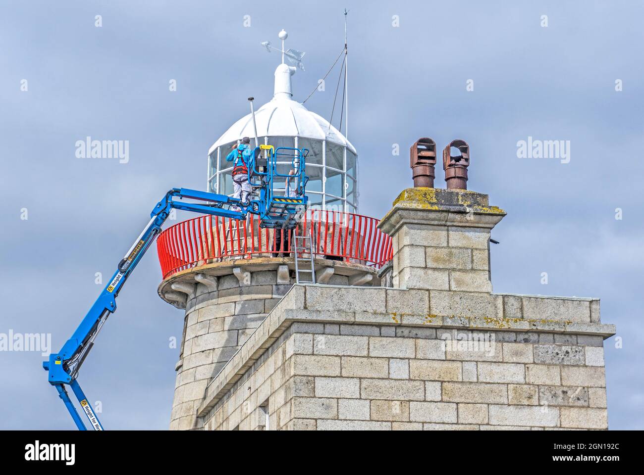 Workmen, using an articulated boom, repainting the lighthouse in Howth, Dublin, Ireland.. Stock Photo