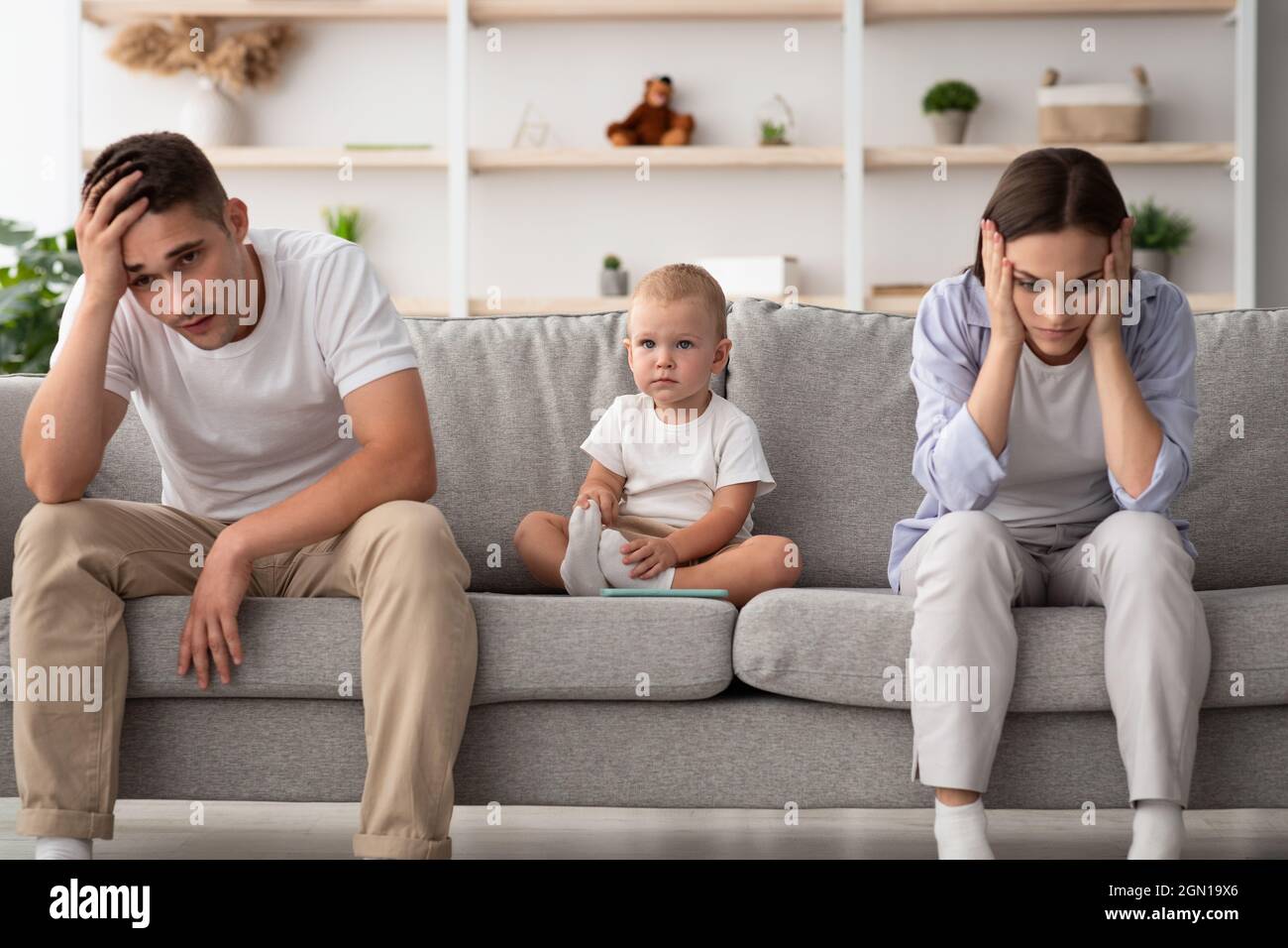 Family Conflicts. Cute infant baby sitting between offended parents after quarrel Stock Photo