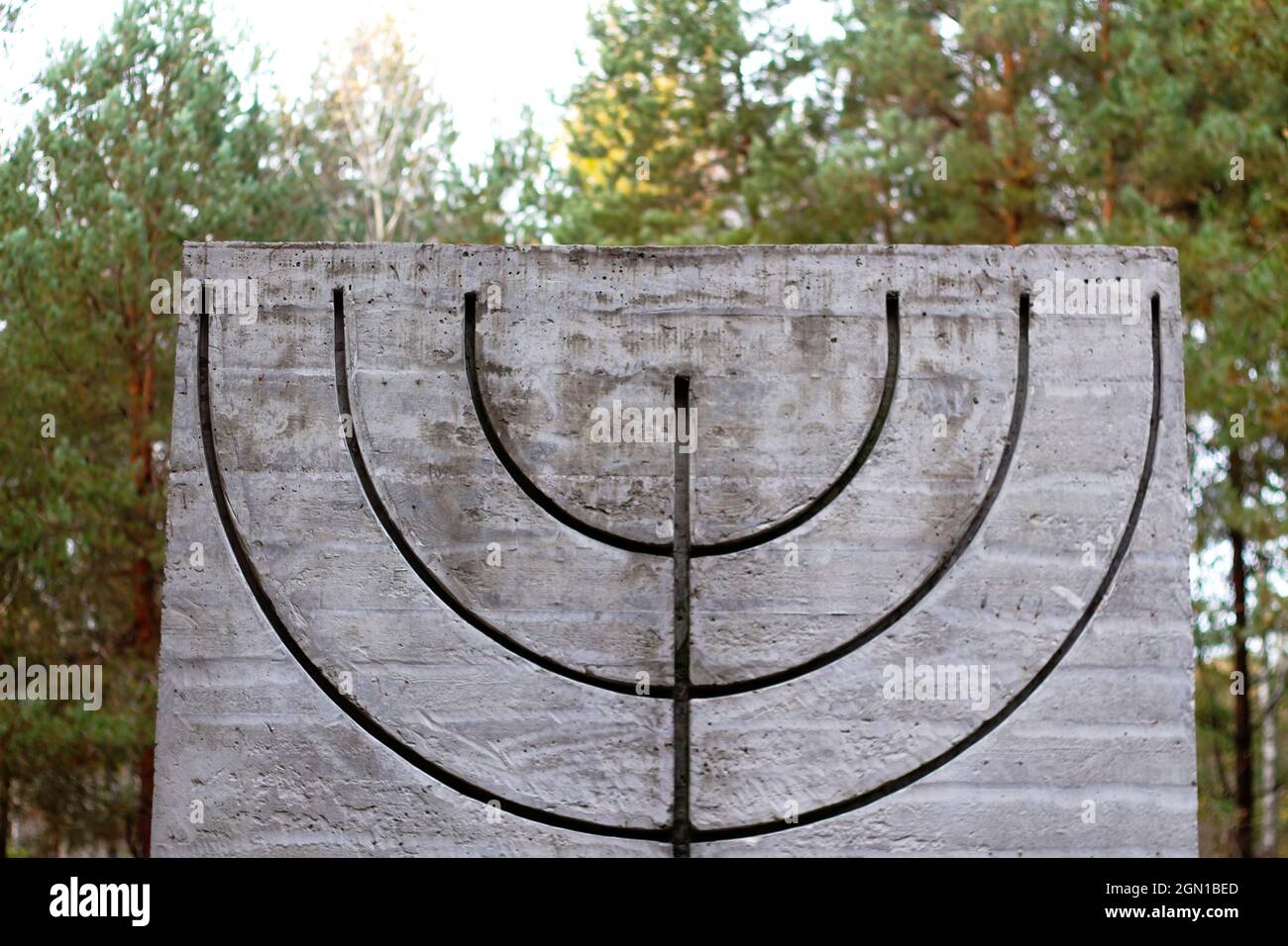Defocus menorah symbol on concrete concrete slab in forest and nature. Symbols of Jewish people. Memory and reverence.Out of focus Stock Photo