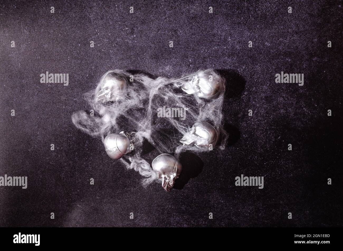 Five silver sculls lying on a dark background, covered with spider web. Halloween horror creative concept. Scary party artistic desing or invitation c Stock Photo