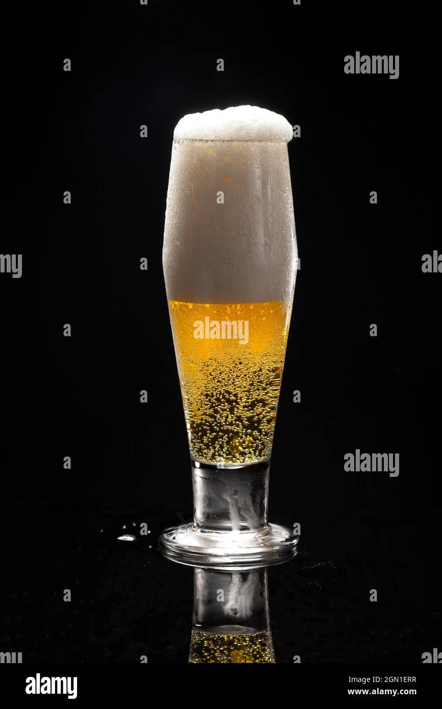 A close up uof a glass of beer against a black background starting to overflow. Stock Photo
