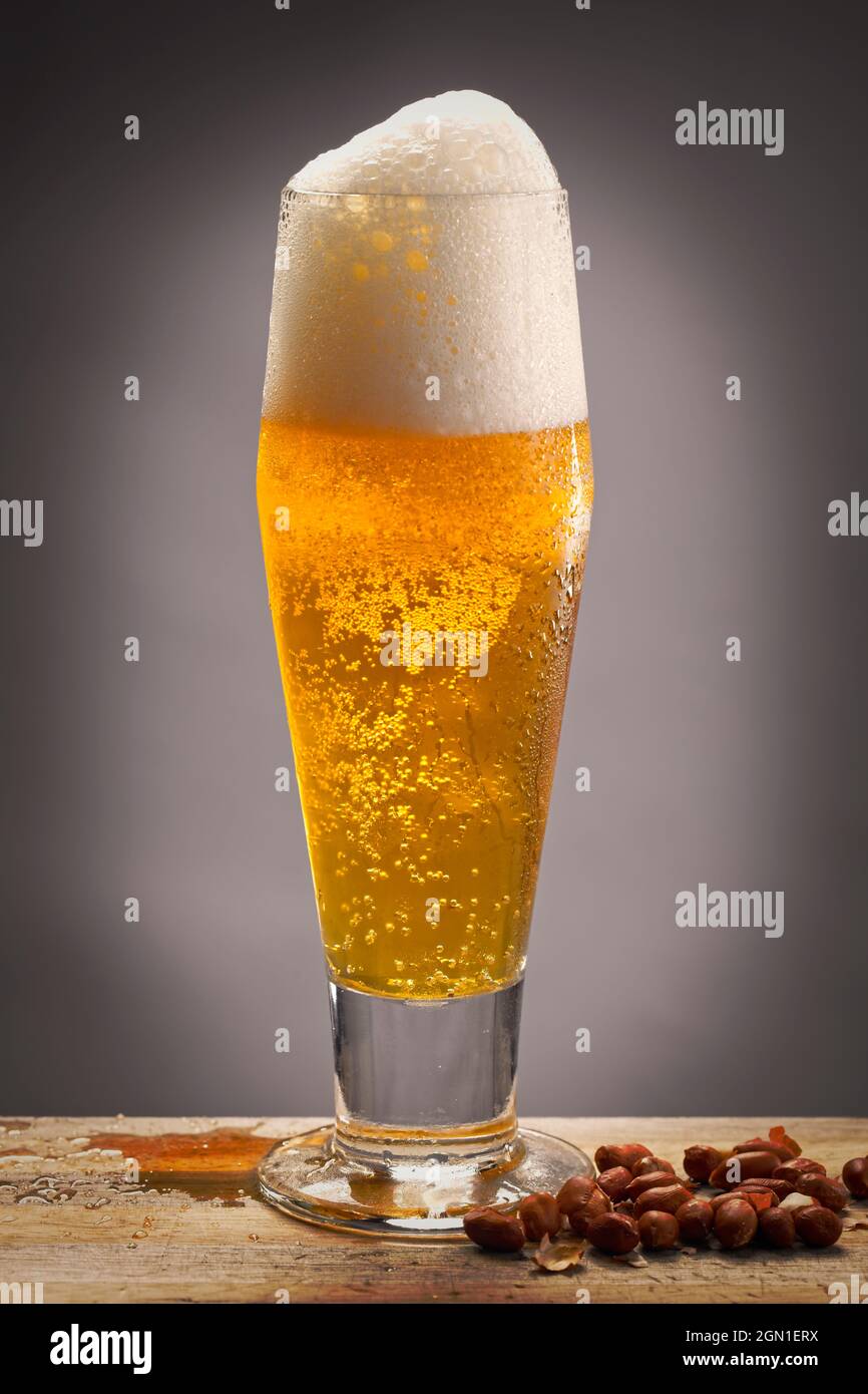 A studio photo of a glass of beer on a wood board and some peanuts next to it. Stock Photo