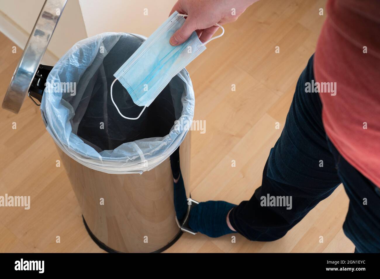 A man throwing a blue disposable surgical mask away into a pedal bin. Concept: anti masker, no face mask, binning face mask, mask debate Stock Photo