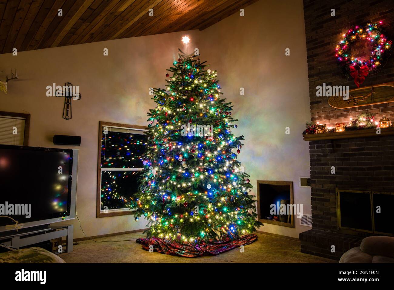 Large Christmas tree lit up in living room with wreath and cross Stock