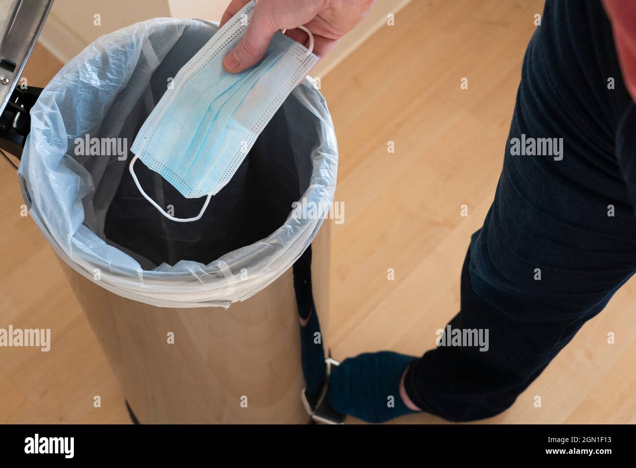 A man throwing a blue disposable surgical mask away into a pedal bin. Concept: anti masker, no face mask, binning face mask, mask debate Stock Photo