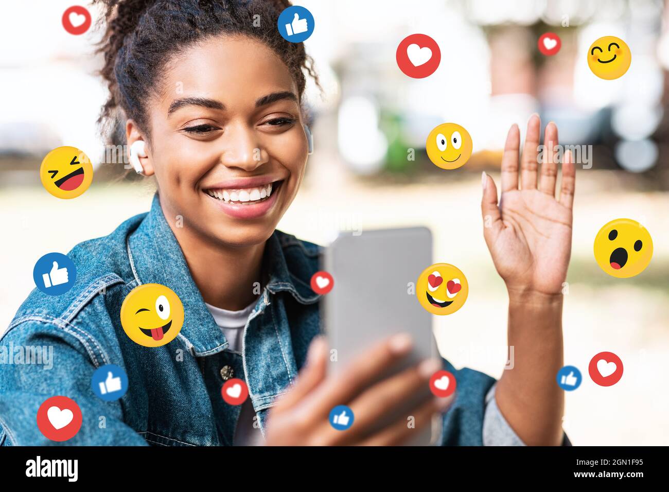 Happy black millennial woman in headphones making video call, double exposure with emoji Stock Photo