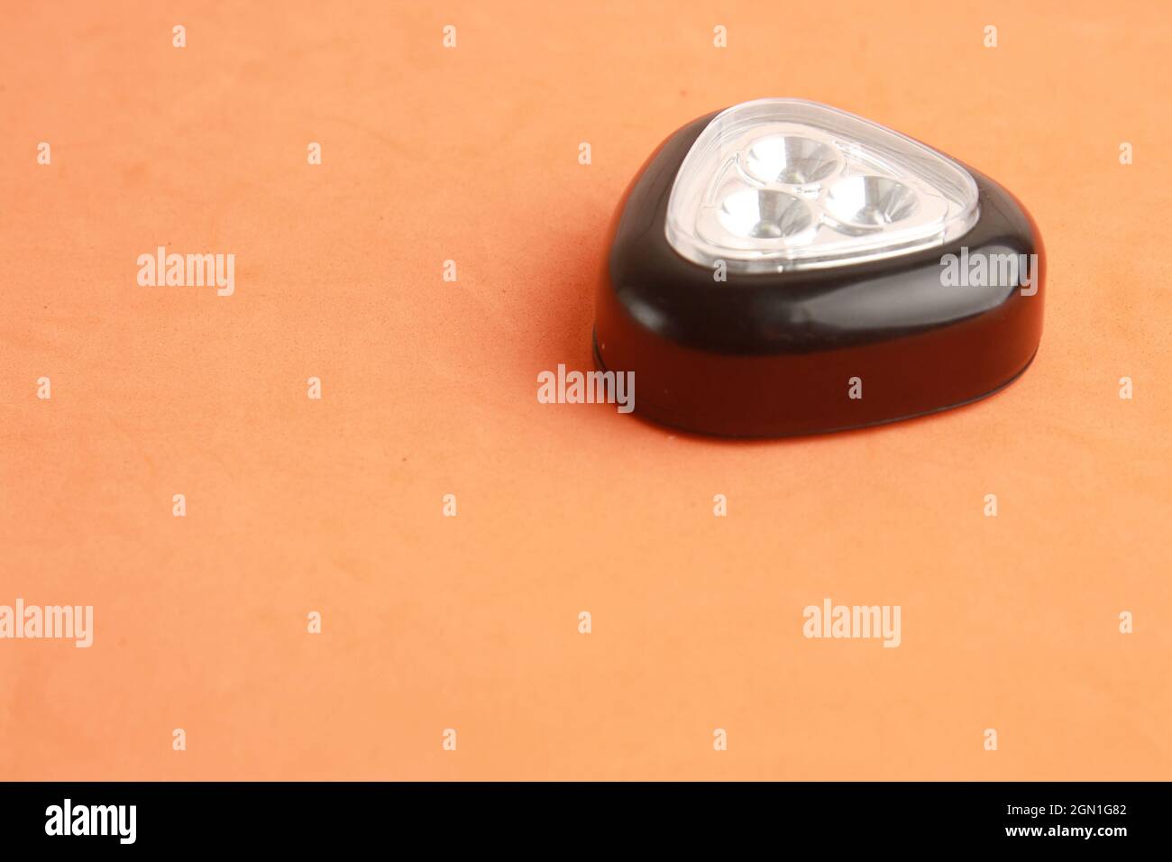 Closeup shot of a triangular black flashlight led light on an orange ...
