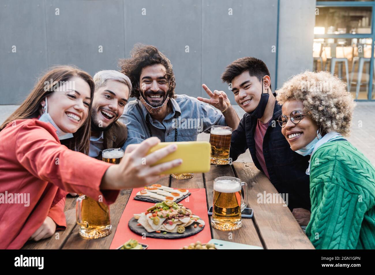 Young multiracial people having fun taking a selfie with mobile phone while drinking beer at brewery bar outdoor - Main focus on asian man face Stock Photo
