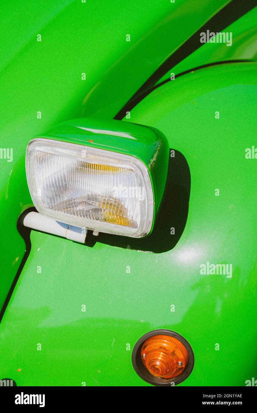 Vertical shot of the headlight of a green vintage car parked outdoors on a sunny day Stock Photo