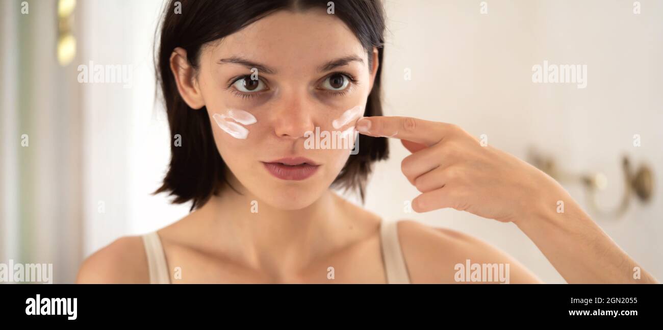 Girl applies cream on her face. Stock Photo