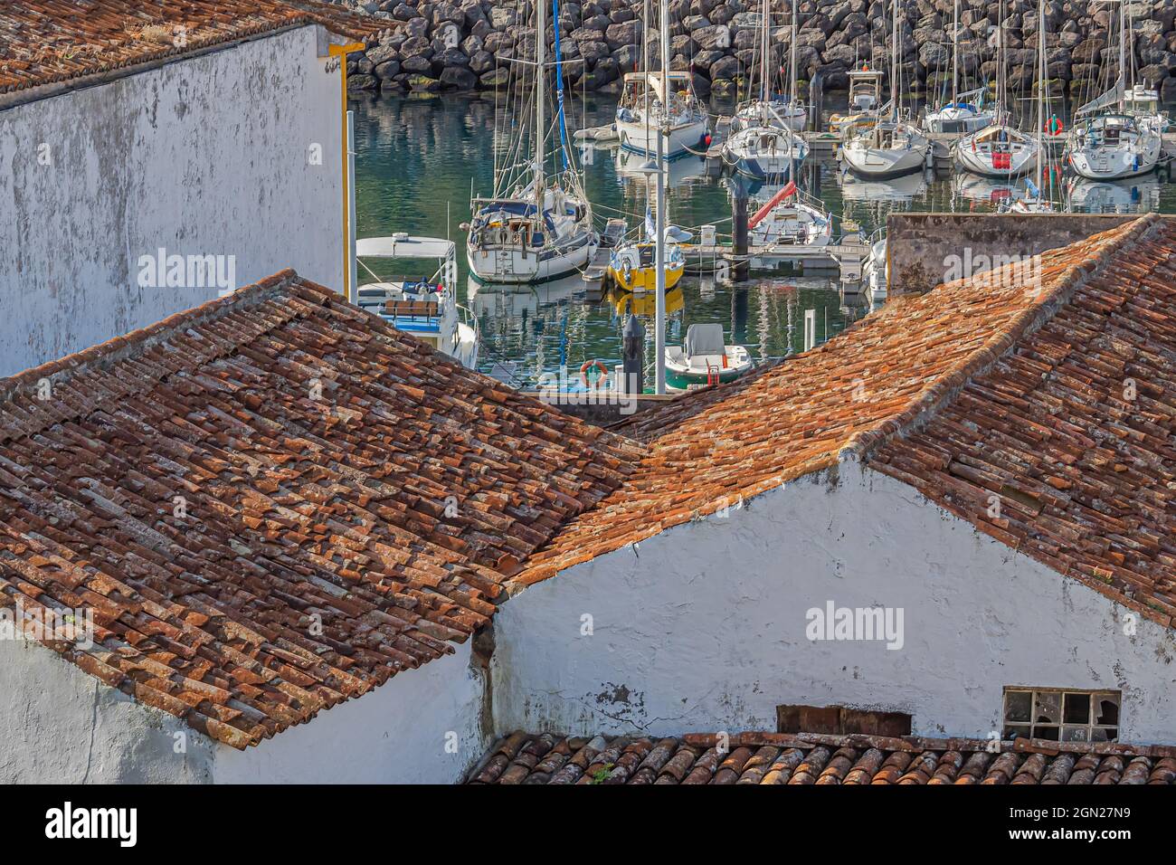 Sailboats in a sheltered marina are visible beyond red tile rooftops on old buildings in the historic city of Angra do Heroismo, Azores, Portugal. Stock Photo