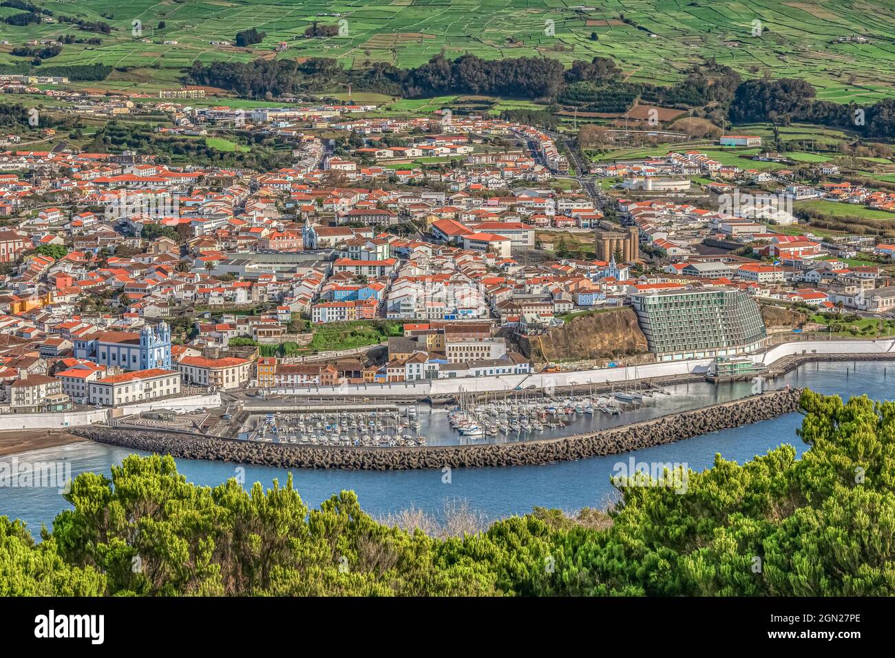 Overview from above of colorful buildings of historic Angra do Heroismo,  marina, and green farmland  as seen from Monte Brasil, Terceira, Azores. Stock Photo