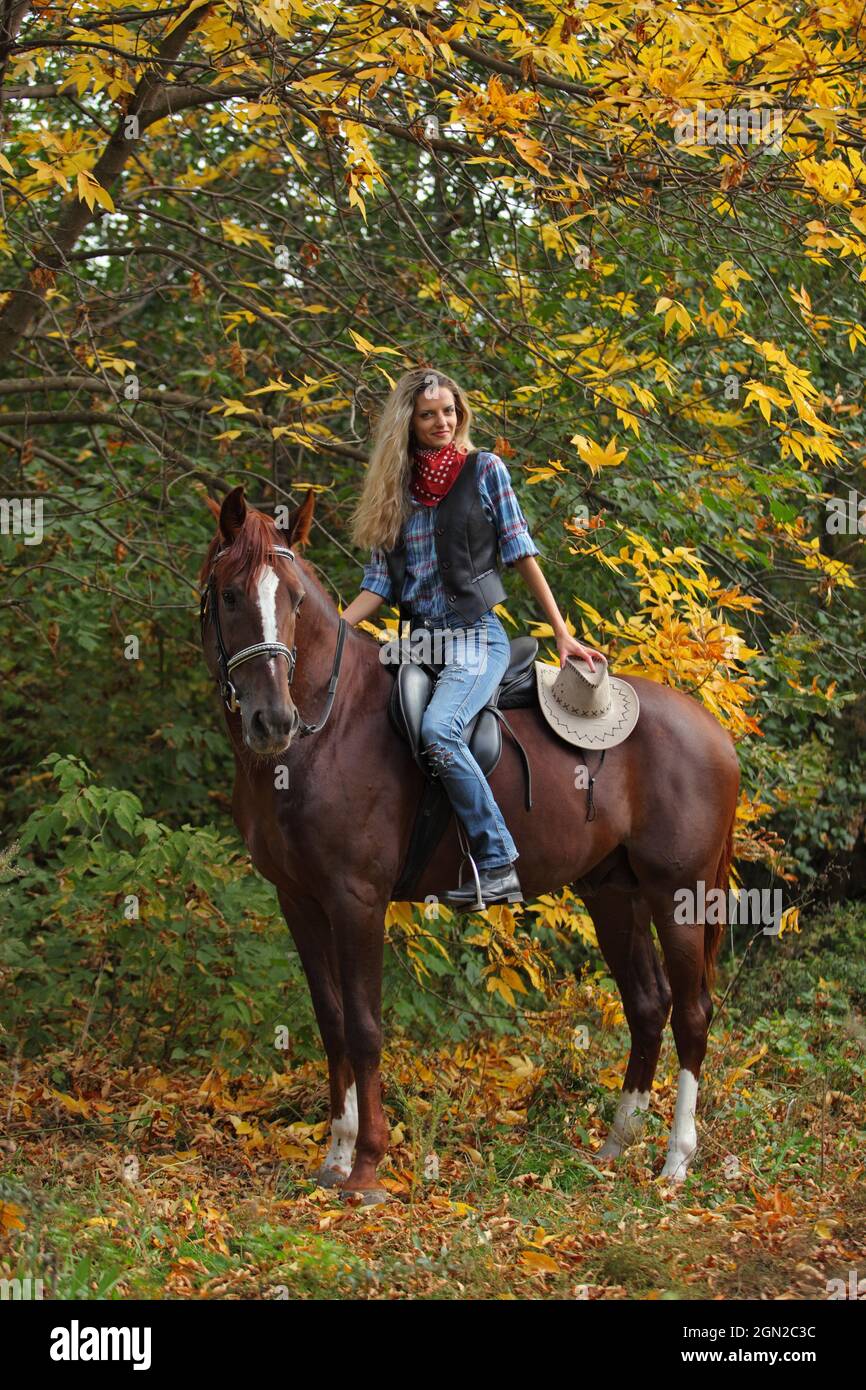 Beautiful cowgirl ride her horse in autumn country road at sunset Stock Photo