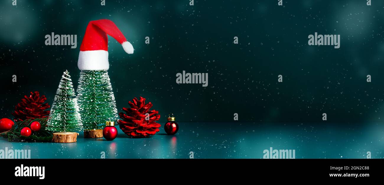 Merry Christmas and happy new year snow falling with xmas tree and red Santa clause hat on dark green background.Banner mockup space for display of pr Stock Photo