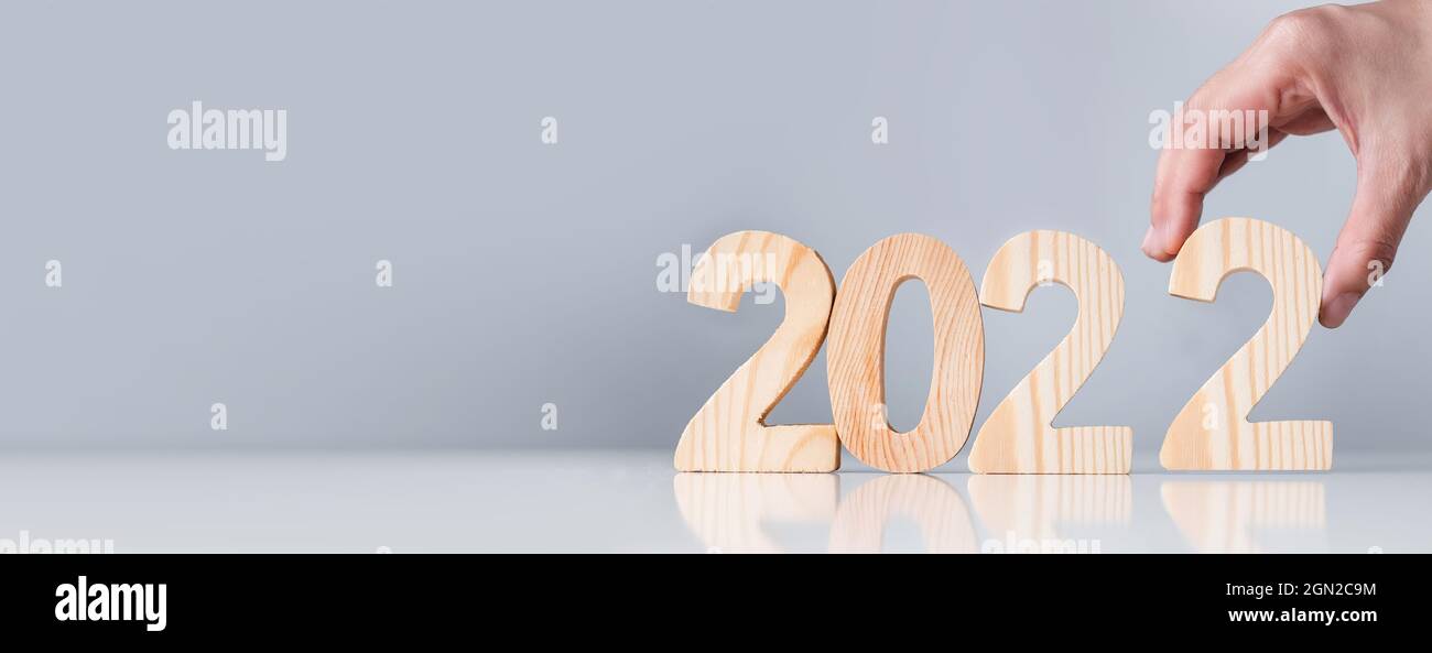 Close up hand pick happy new year 2022 down on white table and grey background.holiday celebration Stock Photo