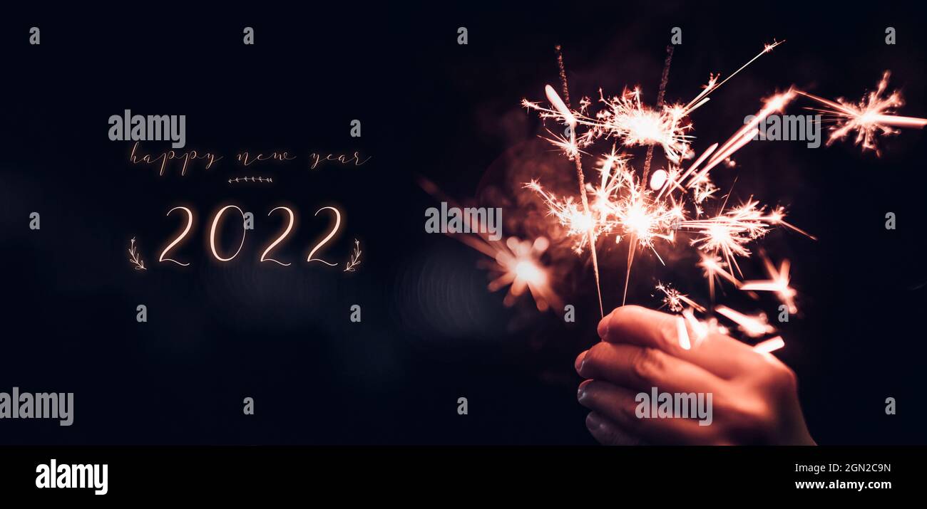 happy new year 2022 text with hand holding burning Sparkler firework blast with on a black bokeh background at night,holiday celebration event party,d Stock Photo