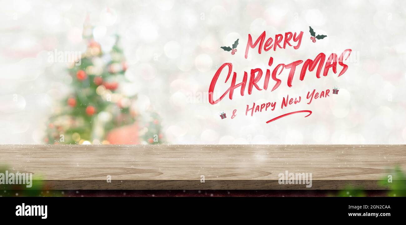 Merry Christmas and happy new year text over wood table top at blur bokeh xmas tree decor with string light background,Winter  greetng card for winter Stock Photo