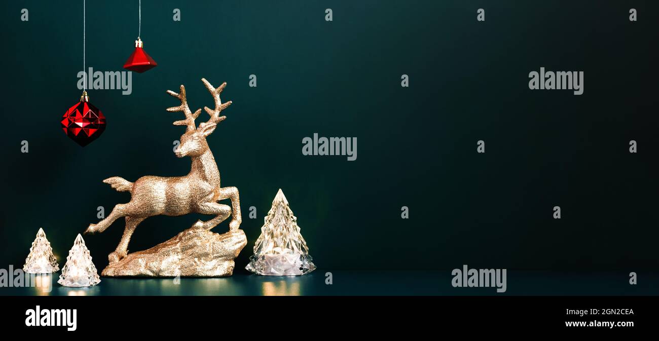 Christmas gold reindeer with xmas tree lamp lights with red baubles hanging on dark blue green background.banner mockup for display of design or invit Stock Photo