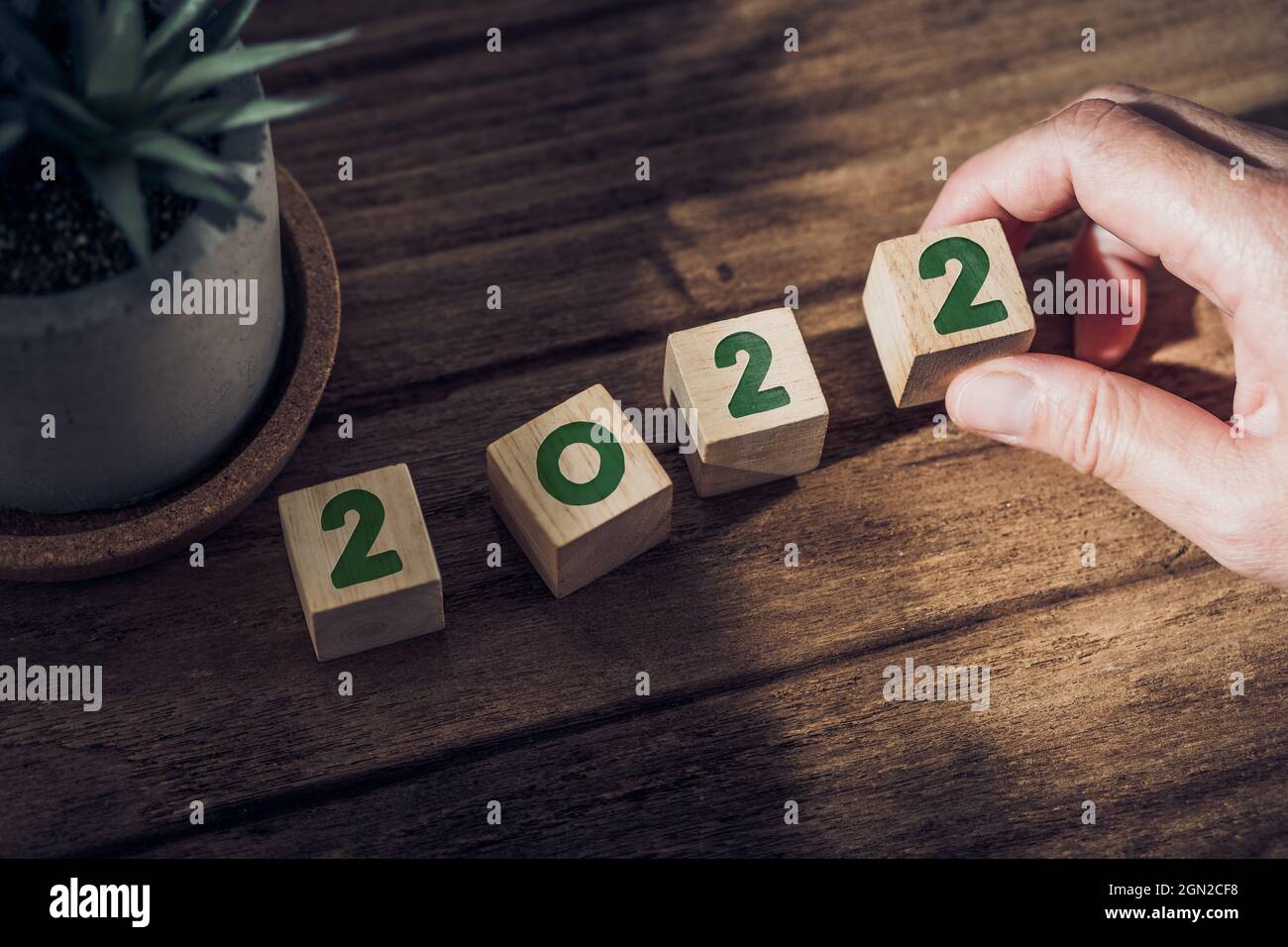 2022 happy new year with hand pick up wood block on wood table with sunlight from window.hope for new year concept Stock Photo