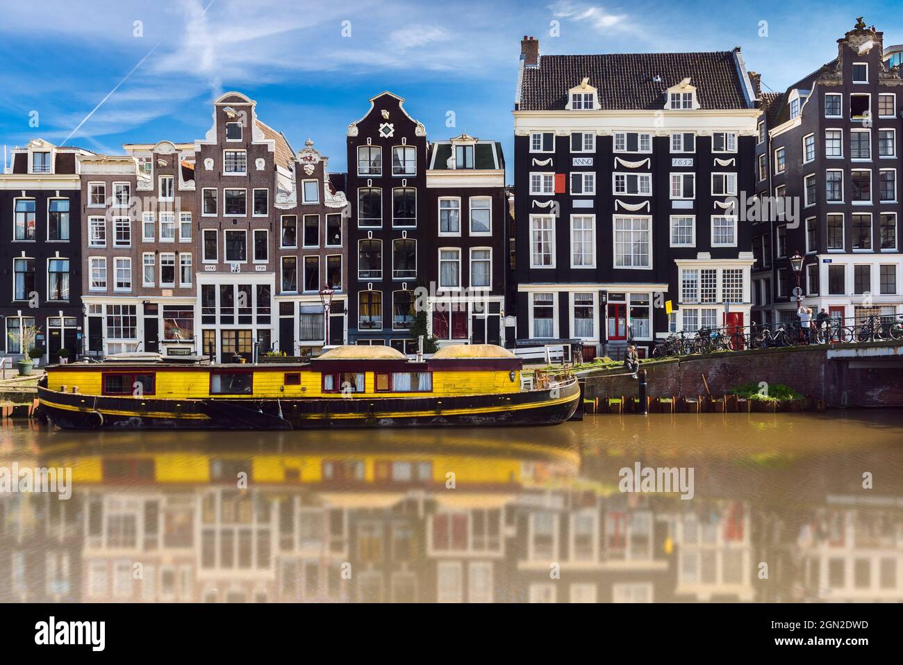 NETHERLANDS, AMSTERDAM, TYPICAL HOUSES ON THE EDGE OF THE CANAL WITH A YELLOW HOUSEBOAT IN THE FOREGROUND Stock Photo