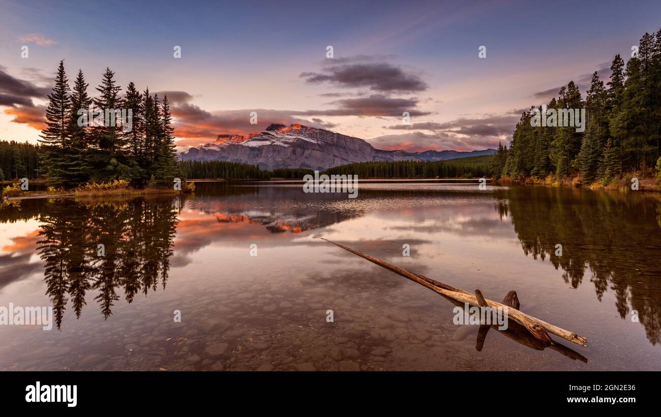 CANADA, ALBERTA, BANFF PARK, TWO JACK LAKE. SUNRISE OVER THE CANADIAN ROCKIES WITH A PIECE OF WOOD IN THE WATER IN THE FOREGROUND Stock Photo