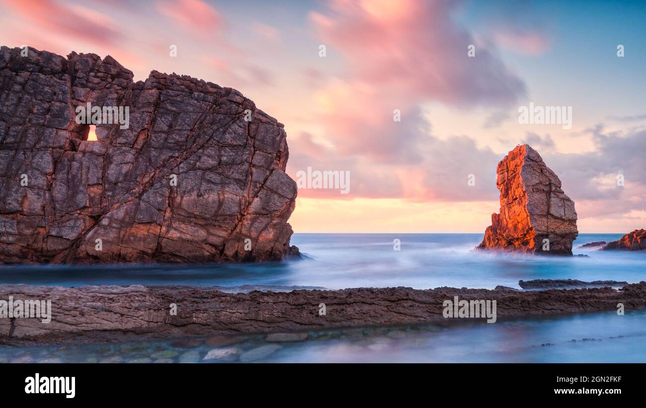 SPAIN, CANTABRIA, LIENCRES. VIEW FROM BELOW OF ARNIA BEACH WITH A CLIFF CARVED OUT BY EROSION AND SHAPED LIKE A SMALL WINDOW AT SUNSET Stock Photo