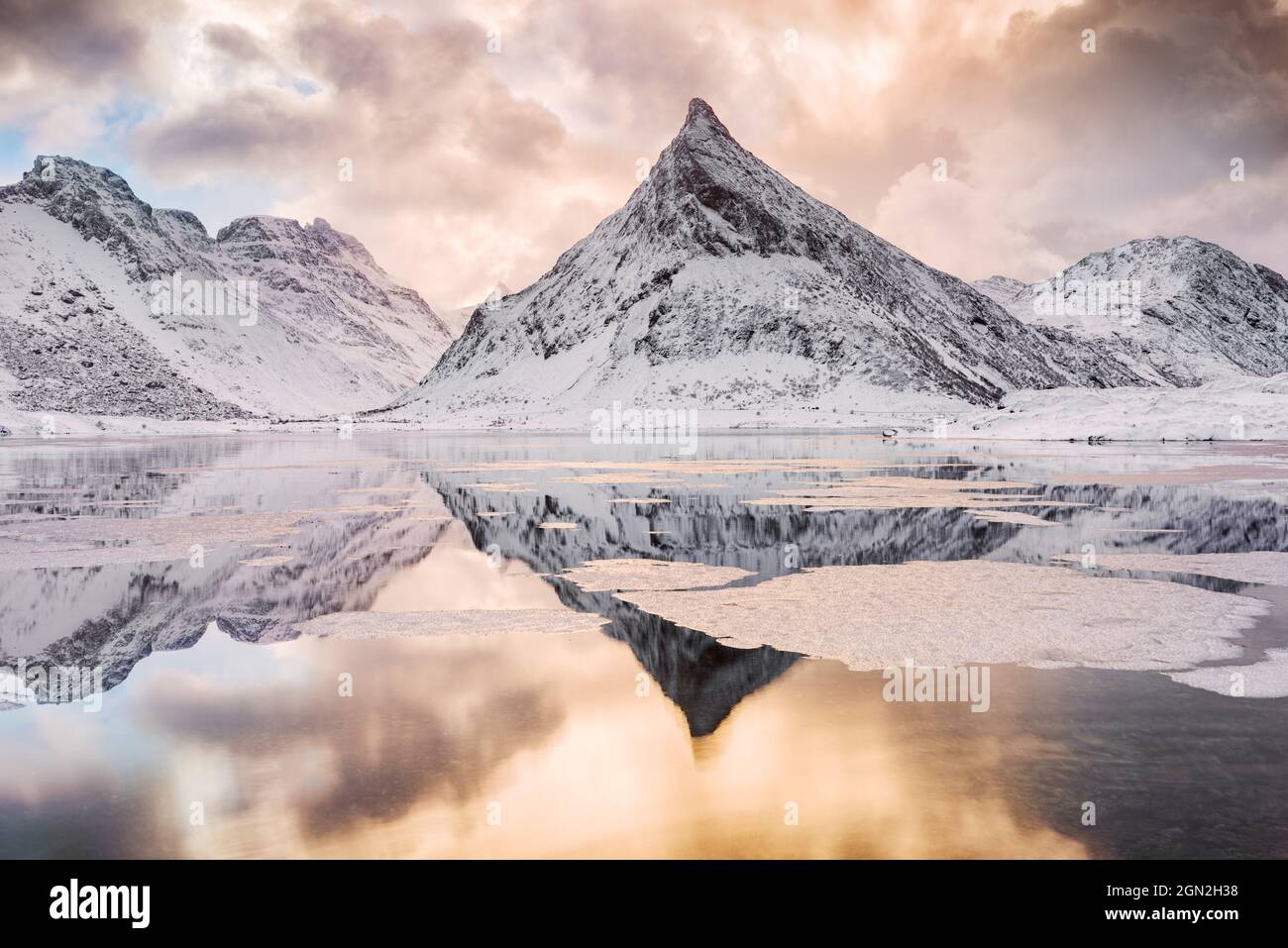 NORWAY, LOFOTEN ISLANDS, FREDVANG. VIEW OF THE SHARP SNOWY MOUNTAIN AT FREDVANG WITH ITS REFLECTION AT SUNRISE Stock Photo