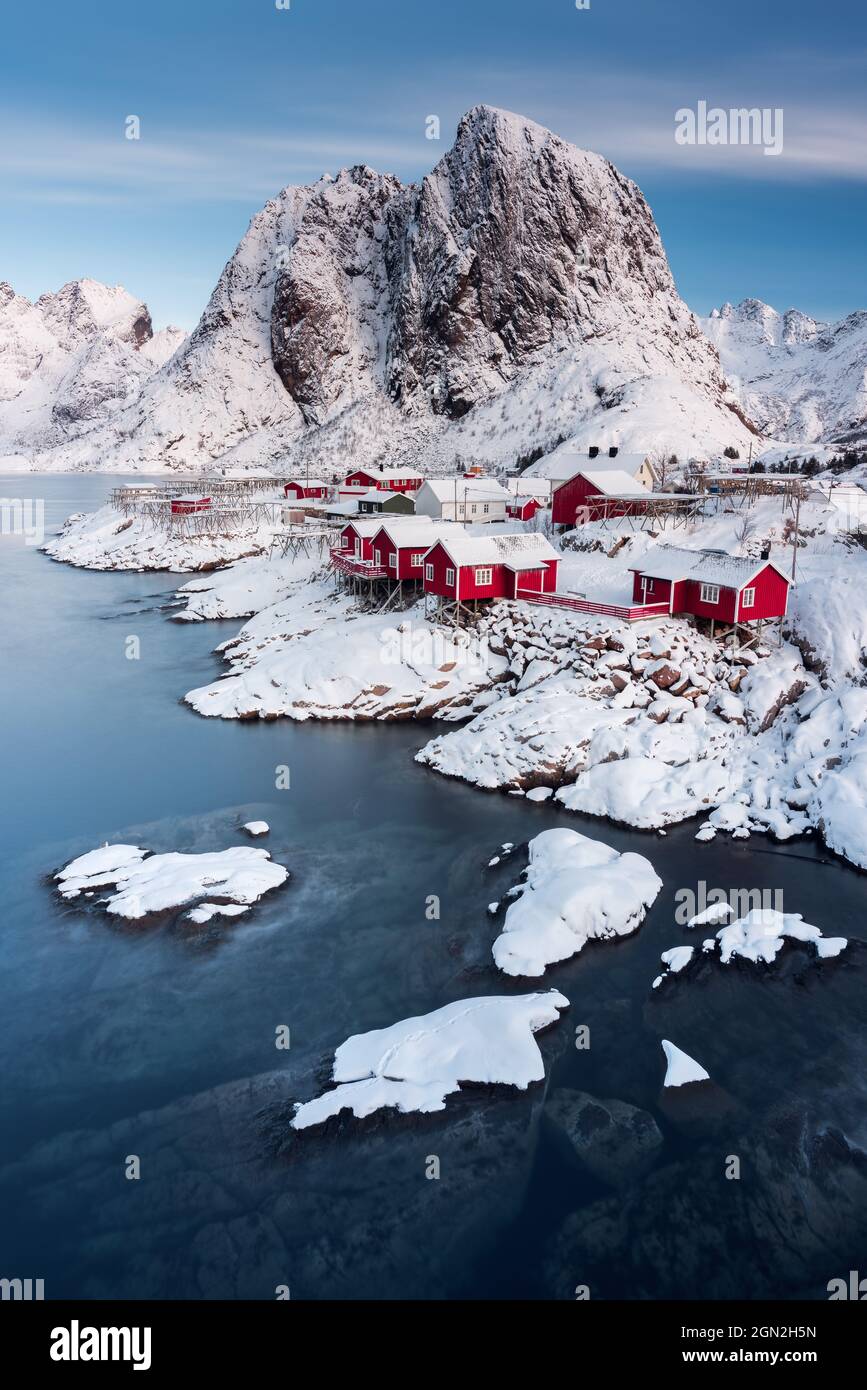 NORWAY, LOFOTEN ISLANDS, HAMNOY, REINE. TRADITIONAL VILLAGE OF FISHING HUTS IN THE SNOW-CAPPED MOUNTAIN CREST OF HAMNOY Stock Photo