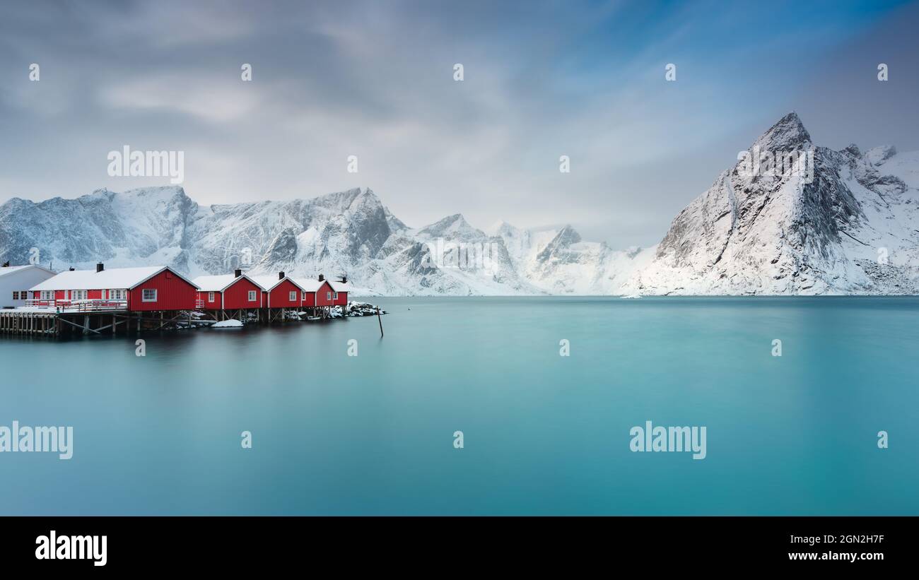 NORWAY, LOFOTEN ISLANDS, HAMNOY, REINE. PANORAMIC VIEW OF FISHERMEN'S HUTS WITH THE SNOW-CAPPED MOUNTAIN RANGE IN THE BACKGROUND Stock Photo