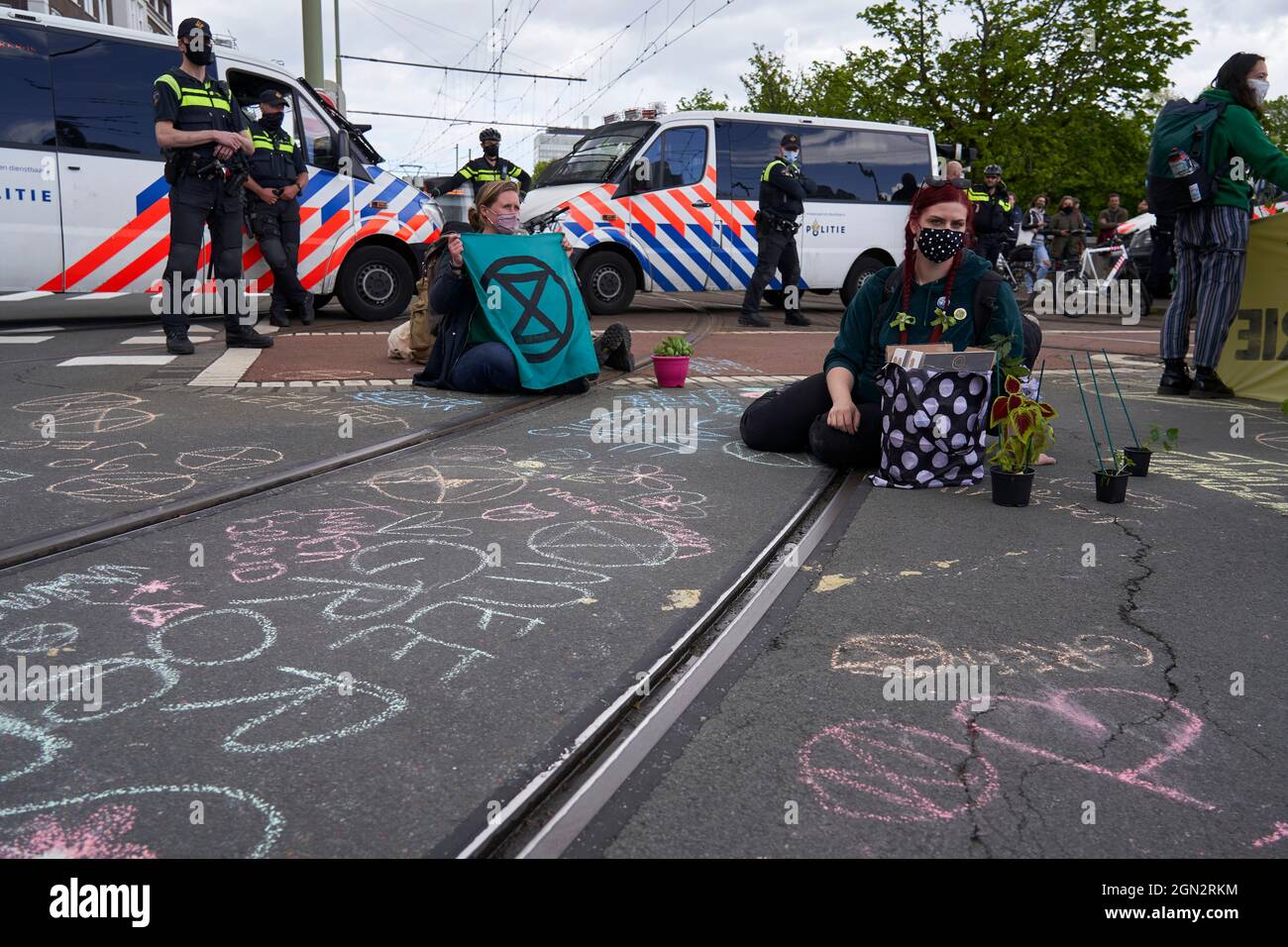 NGO activists, participants in the climate change protest, sit on the ground under police surveillance. Stock Photo