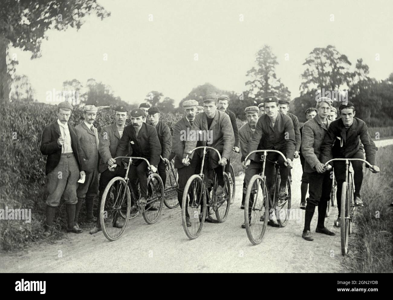 Cycling in Britain in the Victorian age. Here a group of riders are about to set off on a race or time trial on rural backroads c.1900. The starter is on the left and other officials assist each of the eight competitors. The cyclists are wearing surprisingly modern-looking gear with crew-neck sweatshirts or T-shirts and soft leather shoes that have similarities with today’s lightweight trainers. Everyone isa wearing a cap. This is taken from a small image in an old photograph album – a vintage sporting photograph. Stock Photo